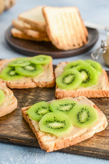 Tasty sandwiches with kiwi and peanut butter on wooden board, closeup