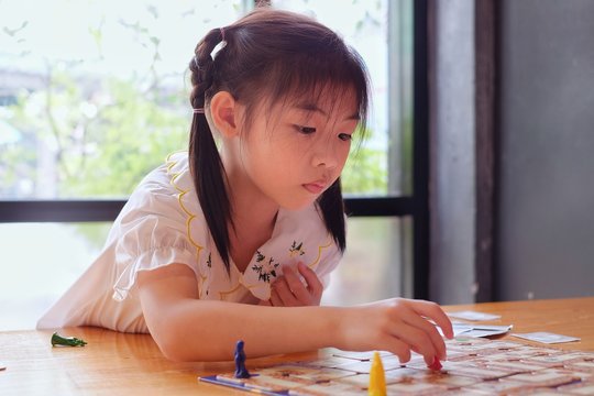 A attractive little Asian girl deep in thought as she contemplates her next move in a board game.