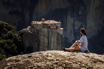 Fototapeta na wymiar tourist woman sitting on the top of mountain on beautiful scenic clif background near Meteora monasteries in Greece.