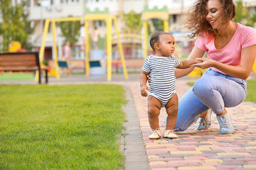 African-American mother teaching her little baby to walk outdoors