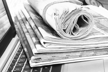 Newspapers and laptop. Pile of daily papers with news on the computer. Pages with headlines, articles folded and stacked on keypad of electronic device. Modern gadget and old journals, focus on paper 