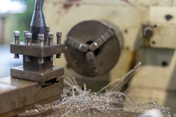 Close up of metal lathe machine carving a piece of cylinder metal with a lot of metal scrap and debris