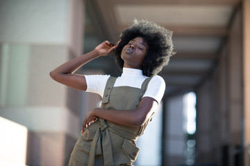 Beautiful African American girl with curly hair, fashionable overalls, and white turtleneck.