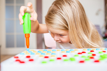 Happy pretty little blonde girl sitting at a table at home playing with a toy screwdriver and multicolor screws. Early education. Close up.