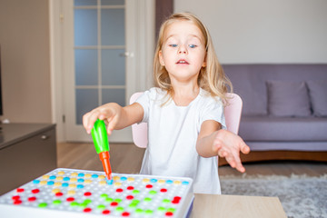 Happy pretty little blonde girl sitting at a table at home playing with a toy screwdriver and multicolor screws. Early education.