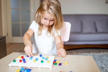 Little blonde girl in a white tshirt playing with plastic multicolor mosaic at home or preschool. Early education concept.