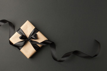 Craft gift box on a dark background, decorated with a textured bow and feathers, creating a romantic luxury atmosphere. For birthday, anniversary presents, gift post cards. - obrazy, fototapety, plakaty