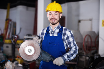 Young smiling male using angle grinder at workplace
