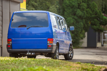 Blue van parked on a city street in rural area.