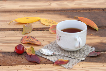 Cup with tea on a background of an old wooden table and autumn leaves of different colors