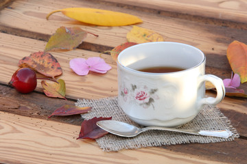 Cup with tea on a background of an old wooden table and autumn leaves of different colors