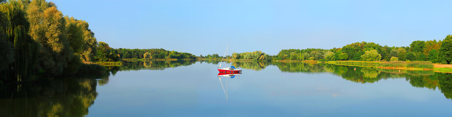 Water of an autumn lake, panoramic view, reflection in calm water. Motor boat with sail