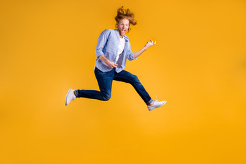 Fototapeta na wymiar Full length body size photo of crazy funny red haired rock hard rocker man fan wearing jeans denim checkered blue shirt sneakers pretending to play guitar jumping isolated vivid color background