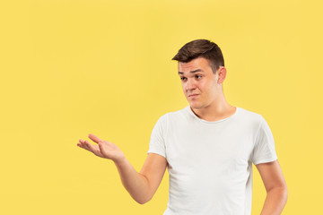 Caucasian young man's half-length portrait on yellow studio background. Beautiful male model in shirt. Concept of human emotions, facial expression, sales, ad. Showing something, looks uncertain.