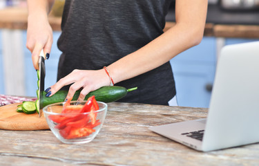 Young girl in a black t-shirt cuts a cucumber on a light wooden board on a gray table in a loft kitchen