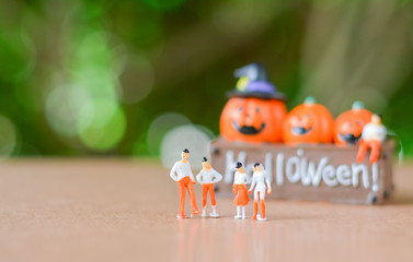 Group of Miniature people, small model human figure standing on floor with blurry pumpkin jack with green bokeh for background. Copy space for your text. Halloween concept.