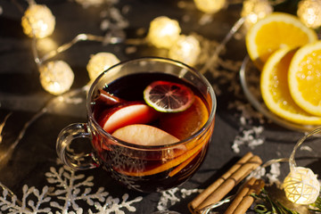 Mulled wine with slice of orange, apples and spices on christmas background with different decorations. Hot christmas drink.