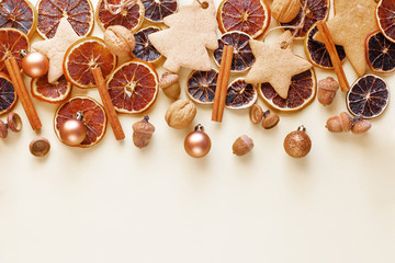Obraz na płótnie Canvas Dried slices of oranges, gingerbread, cinnamon sticks, acorns, nuts and christmas balls for holiday decoration. Christmas or new year decor on a light beige background. Holiday background. Copy space