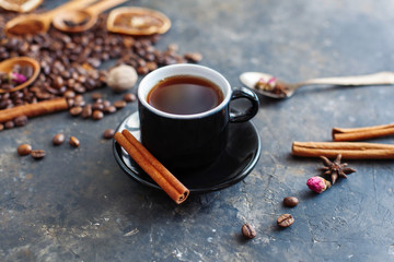 A cup of aromatic black coffee with a cinnamon stick on a saucer, americano or espresso. Coffee ingredients in the background. Dark textured creative surface. Close up, selective focus.