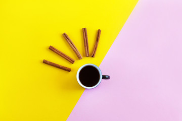 Creative flat lay, cup with black coffee or tea and cinnamon sticks on a bright pink and yellow...