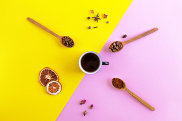 Ingredients for aromatic coffee around a cup of americano or espresso. Spices, ground coffee and coffee beans in wooden spoons. Bright pink and yellow paper background. Top view.