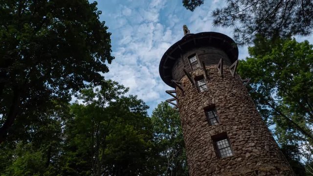TIMELAPSE: Rolling clouds, a blue sky, and  trees surround a large stone tower.