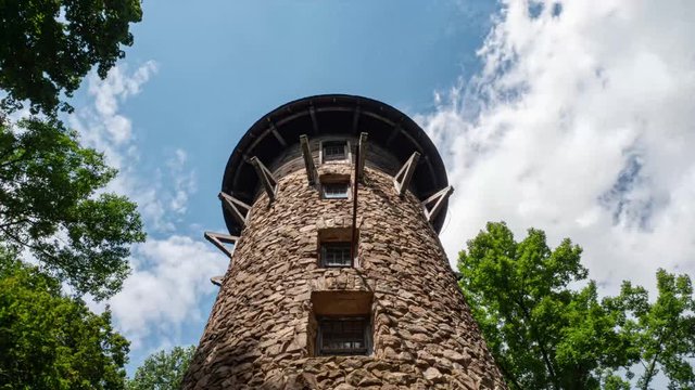 TIMELAPSE: Rolling clouds, a blue sky, and  trees surround a large stone tower.