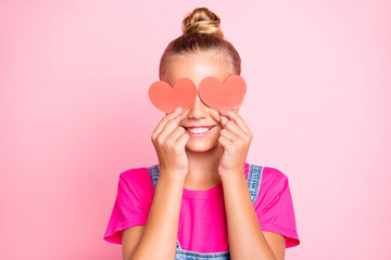 Close up photo of cheerful funky little girl hiding her eyes behind red heart shapes smiling...