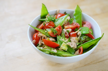 snow peas and cherry tomatoes with tuna as a healthy salad for low carb diet in a white bowl on a wooden table, copy space