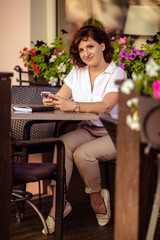 young beautiful girl in a white strict shirt with a phone in her hands sits in a summer cafe
