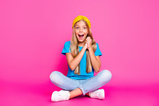 Full body photo of amazed excited funny funky kid wait for desirable present scream wow omg sit with crossed folded wear blue t-shirt sneakers isolated over pink color background