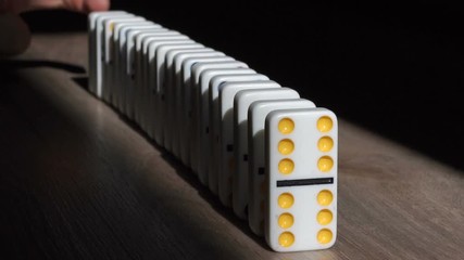 A men pushes a Domino and starts a chain reaction on the floor in a patch of sunlight. Sun ray. Close-up. Slow motion. Dominoes. Chain reaction. The Domino Principle. Board game. Falling dominoes.