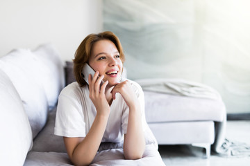 Young happy smile woman phone call on sofa in living room, at home. Excited girl lying talking cellphone