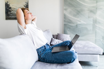 Beautiful young woman with laptop and cup of coffee on the sofa