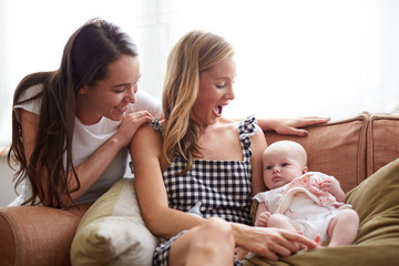 Obraz na płótnie Canvas Loving Female Same Sex Couple Cuddling Baby Daughter On Sofa At Home Together