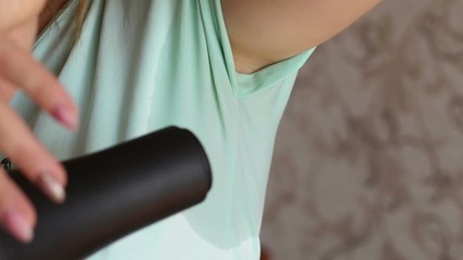 Woman drying wet armpit using hair dryer. Getting rid of sweat and bad smell, hyperhidrosis. Woman with sweat stain on her clothes under armpit is drying her armpit with hair dryer.