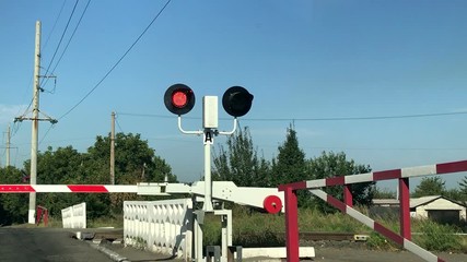 Close-up of red flashing traffic lights at a railway crossing with a lowered barrier. Railroad crossing with barriers lowered and red lights flashing warning and announcing coming train on sunny day.
