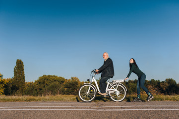 Young caucasian girl on roller skates and a man on a electric bike fun ride together. Active leisure and hobbies. Father and daughter.