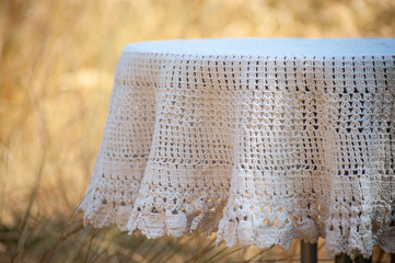 Closeup of white crotchet tablecloth on a round table on yellow grass background
