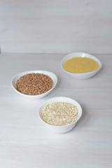 three cereals-buckwheat, oatmeal and millet. in white plates on a wooden background. healthy diet. full diet food