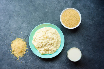 millet porridge in a plate on a dark background and ingredients-millet and milk in a glass.