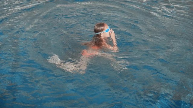 Teenager girl in googles swimming in floating pool. Happy girl swimming in blue water pool at resort hotel. Girl diving underwater in swimming pool