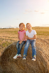happy children sitting on haystack at sunset. kids, girl with boy sitting in field