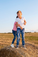 Naklejka na ściany i meble happy children jostling on haystack at sunset. kids, girl with boy standing in field