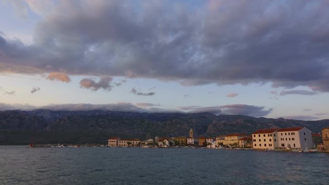 Day to night timelapse of small coastal town and harbor, mountains and rolling clouds in the background, colorful sunset in Dalmatian town Vinjerac, Croatia