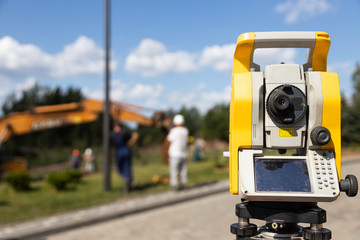 Close-up of yellow and orange tacheometer standing on street against work on construction site