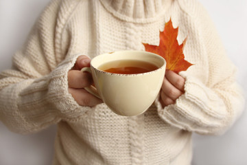 cup of hot fragrant tea and a red maple leaf in a woman's hands, knitted sweater texture, close-up, copy space, autumn mood concept