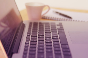 black laptop keyboard with selective focus and blur close-up, side view, a cup of coffee and a notebook from the back, soft pinking, horizontal