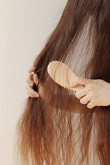 girl with long hair combing them with a wooden comb, holding strands, horizontal, close-up