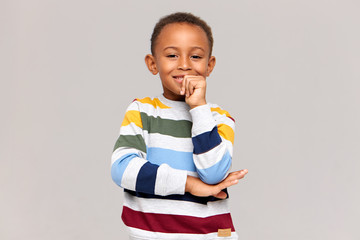Joy, happiness and childhood concept. Handsome cheerful African American little boy wearing stylish multicolored jumper laughing, holidng hand at his mouth, having happy joyful facial expression © Anatoliy Karlyuk
